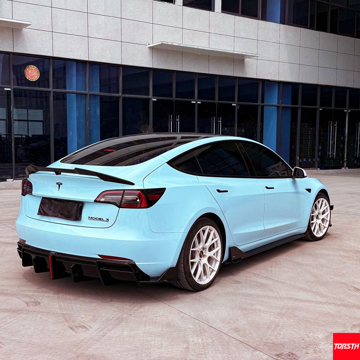 Light blue Tesla Model 3 parked in front of a modern building