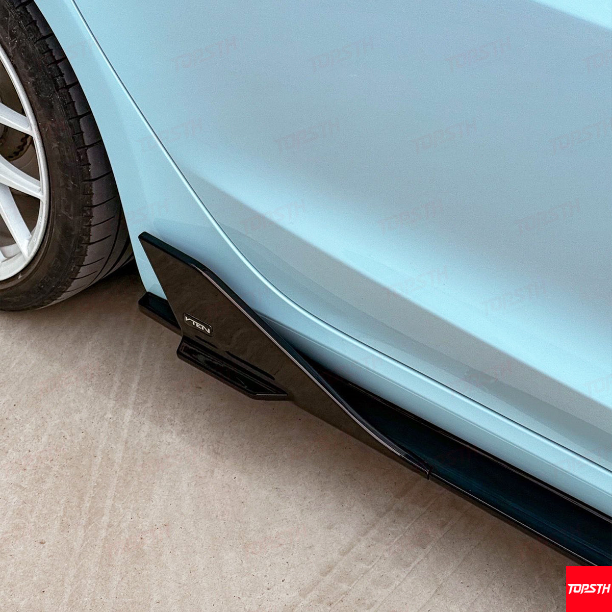 Car side skirt extension attached to a light blue car on a concrete surface