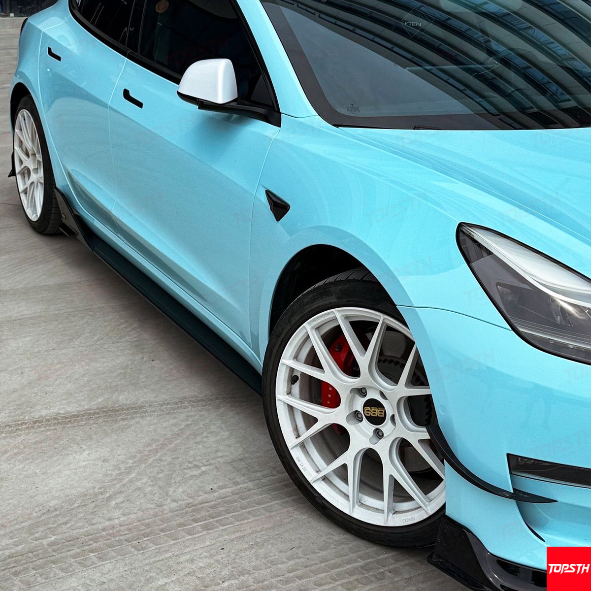 Side profile of Tesla Model 3 featuring performance side skirts and white multi-spoke wheels.