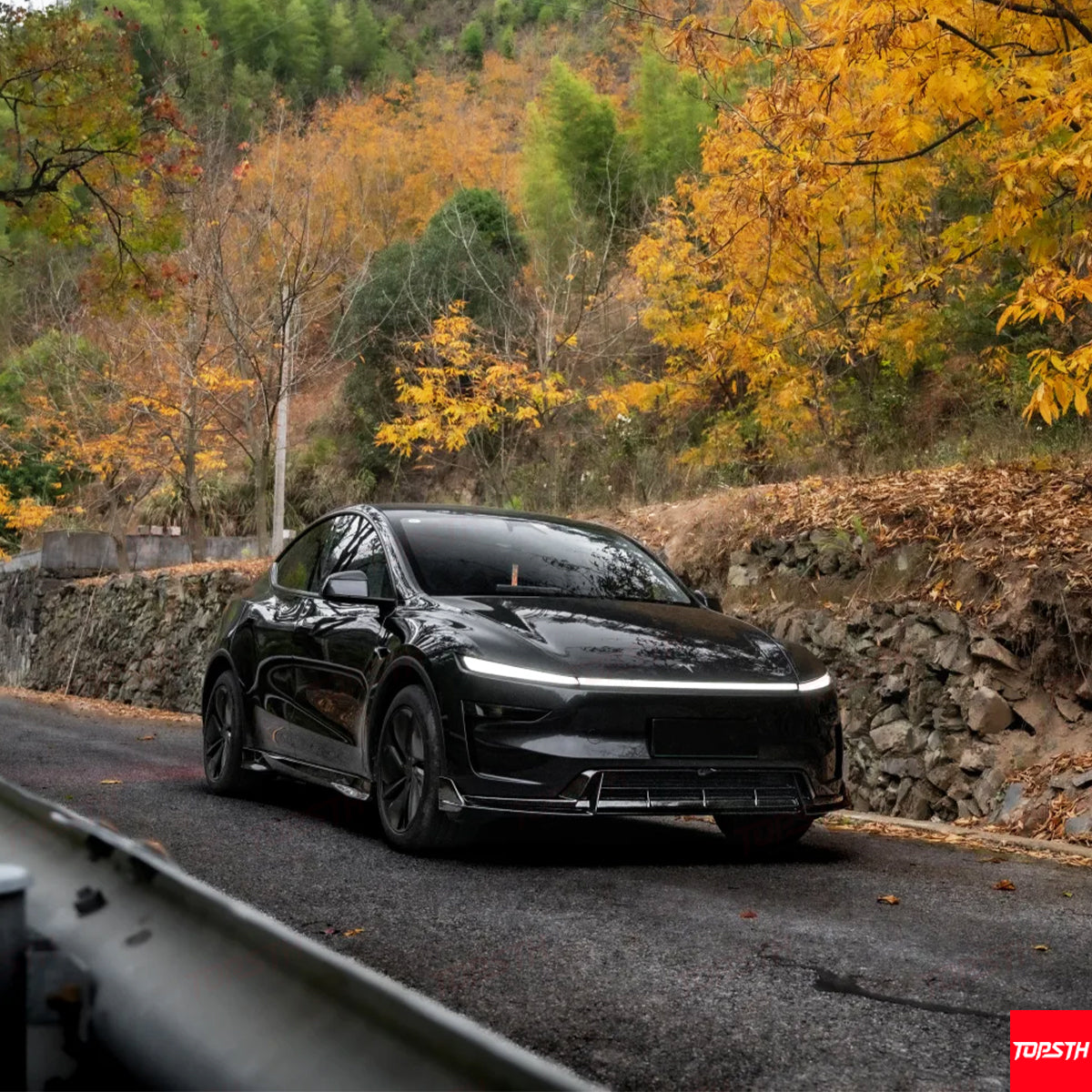 Custom black Tesla Model Y with a wide body kit parked on a scenic mountain road during autumn.