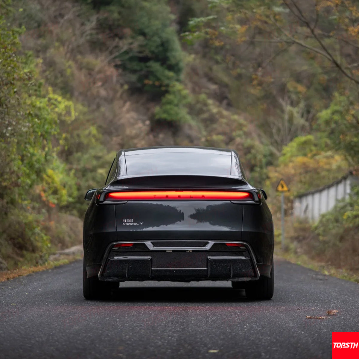 Direct rear view of a black Tesla Model Y displaying the horizontal light bar and sporty rear wing.