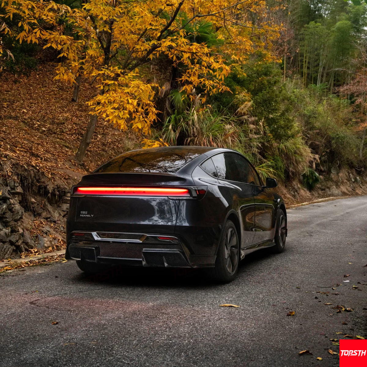 Rear three-quarter view of a black Tesla Model Y featuring a continuous LED taillight and performance rear diffuser.