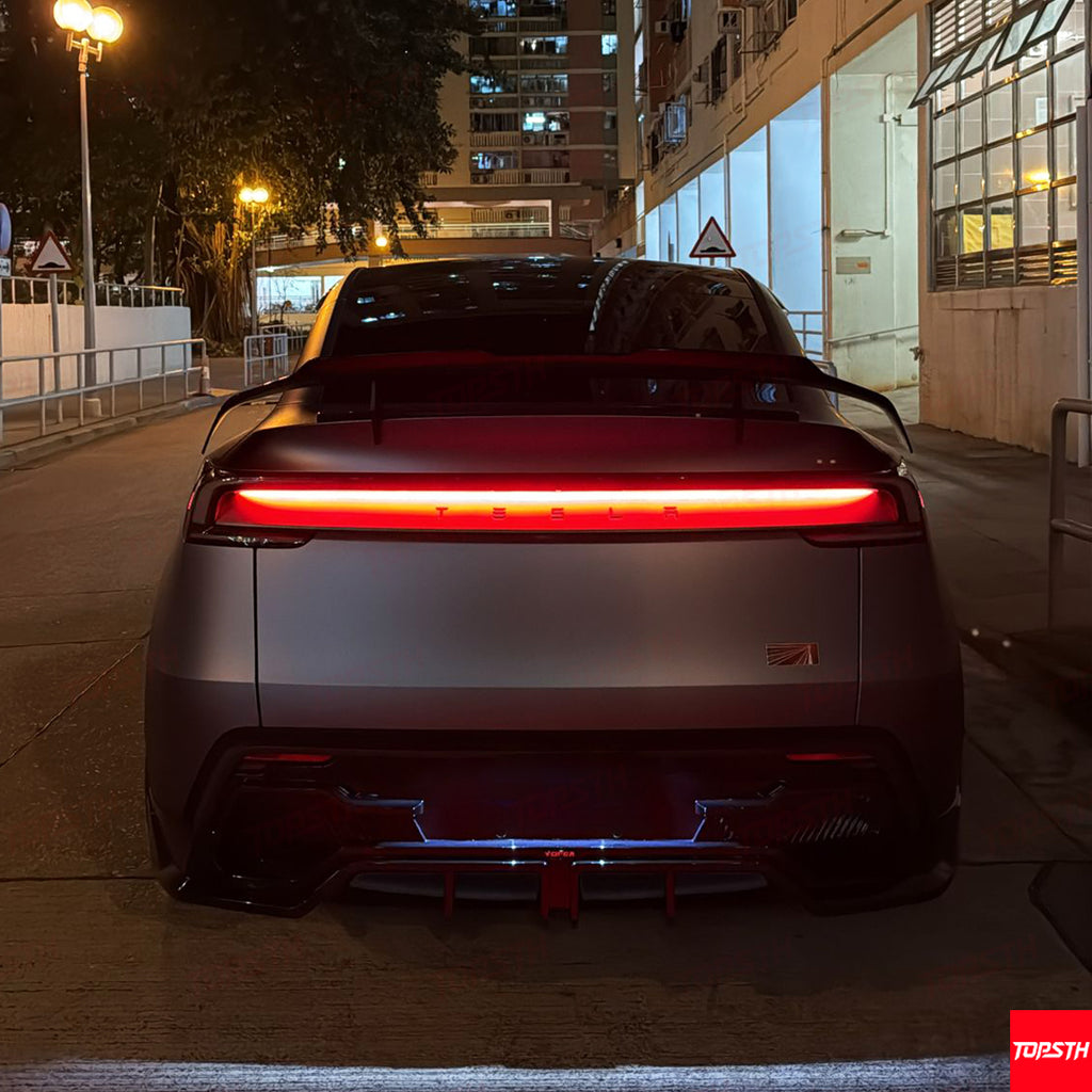Sleek rear silhouette of a Tesla Model Y featuring a carbon fiber wing and illuminated taillights at night.