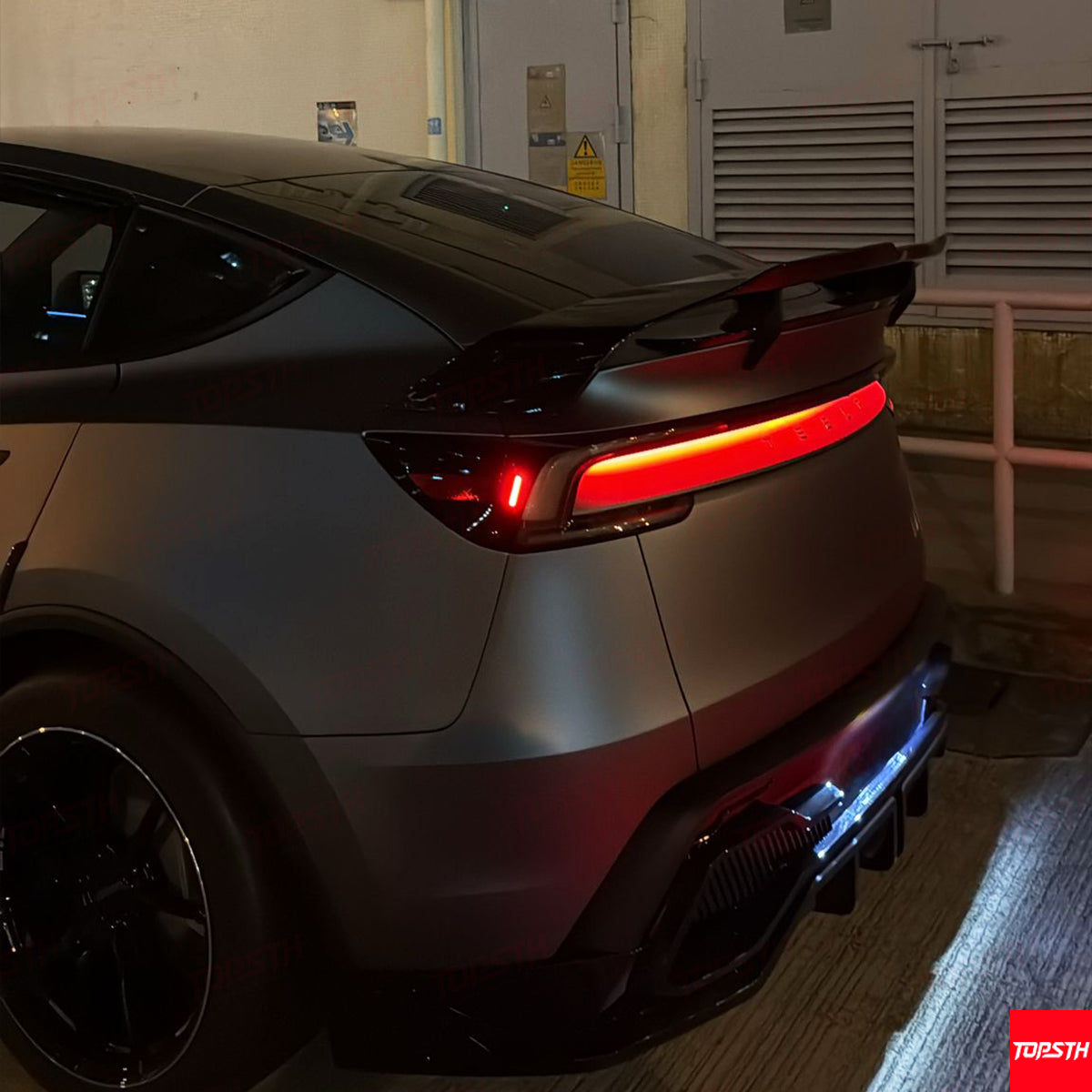 Modified Tesla Model Y with a racing-inspired carbon fiber spoiler and aggressive rear diffuser.